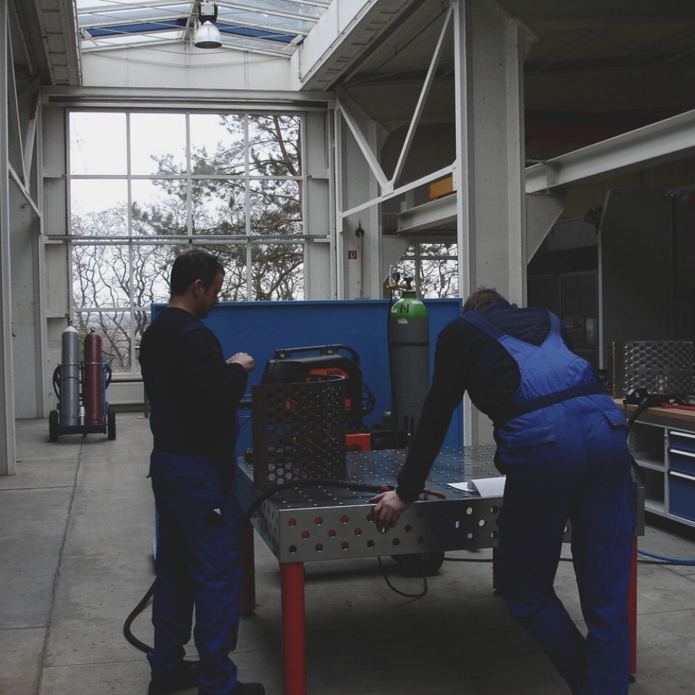 Mitarbeiter bei CUTMETALL bearbeiten einen gelochten Siebträger für Recyclingmaschinen an einem Schweißtisch