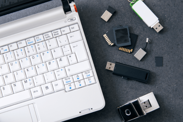 Ein weißer Laptop auf einer grauen Oberfläche, daneben mehrere USB-Sticks, SD-Karten und Adapter.