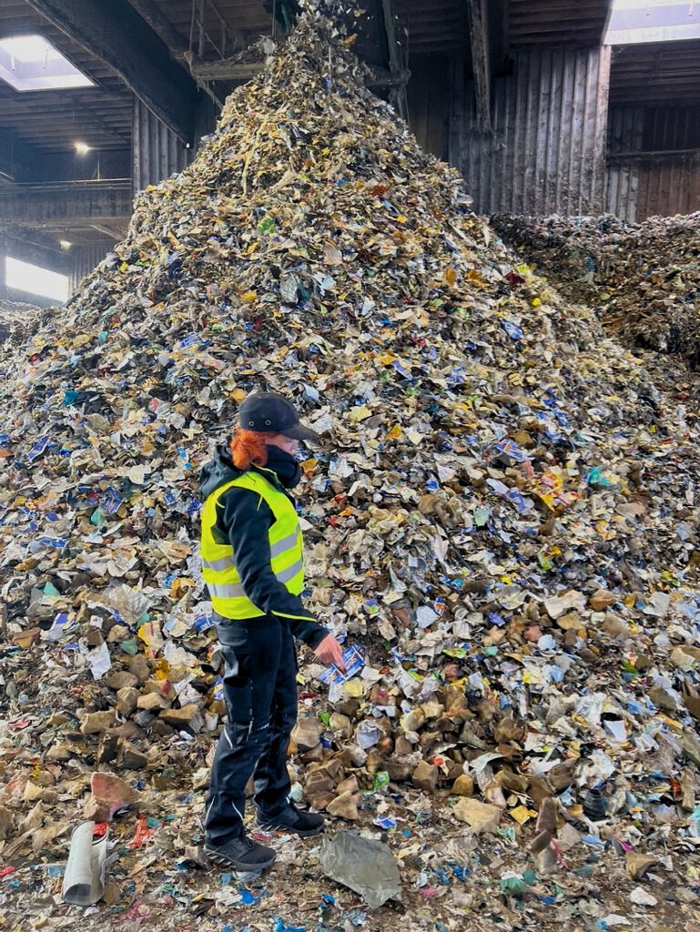 Employée inspectant un important tas de déchets plastiques mélangés dans une installation de recyclage – matière d’entrée typique pour les broyeurs industriels