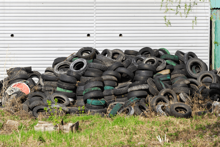A pile of old tyres is stacked in front of a warehouse.