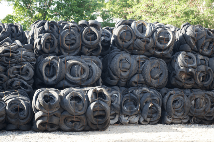 On a sunny day, with trees in the background, worn-out tyres are stacked into cubes and lined up side by side