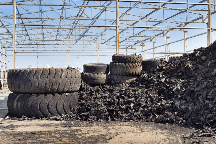 Stacked used tyres next to shredded ones. In the background, a steel framework and blue sky can be seen.