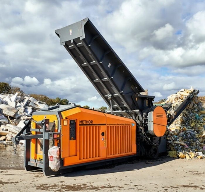 Industrial machine in front of a mountain of garbage with old mattresses and co.