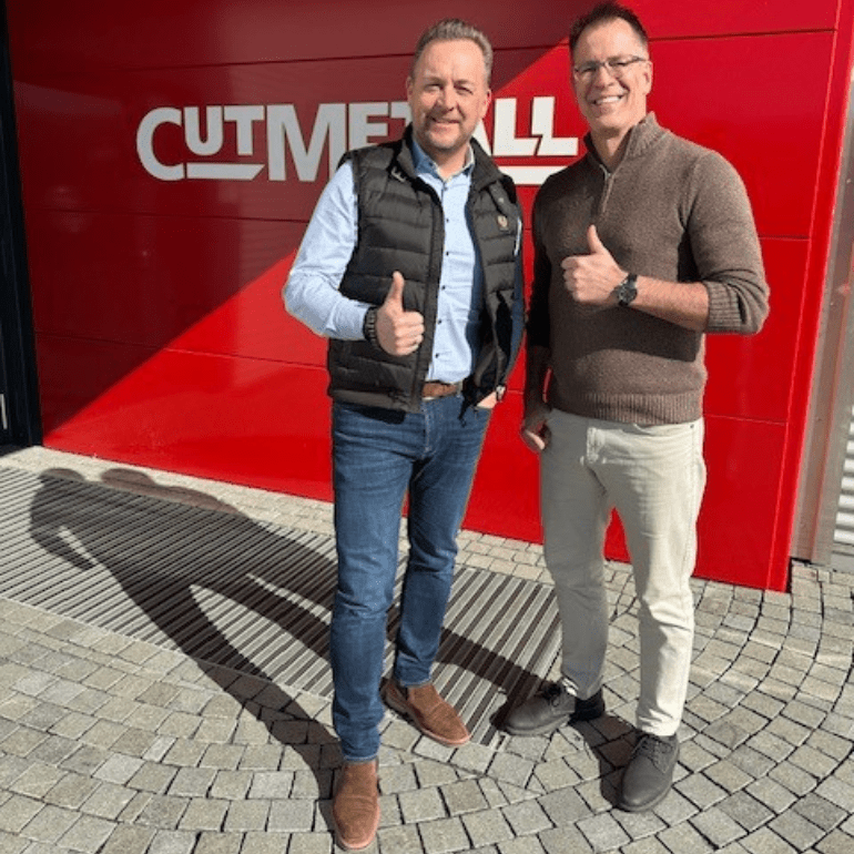 Christian Hoffmann und Paul Hueter zeigen die Daumen hoch vor dem CUTMETALL logo auf einer roten Wand