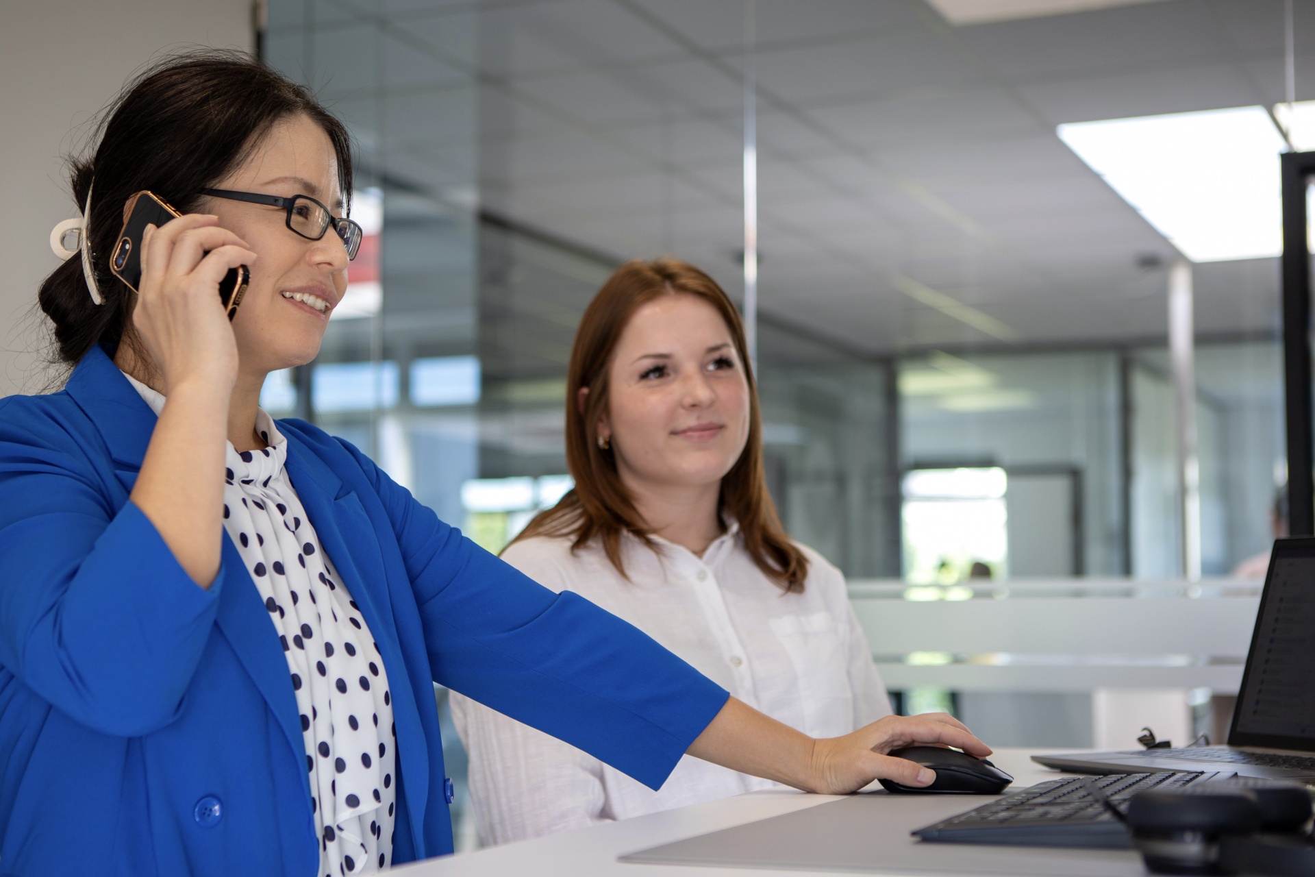 Zwei CUTMETALL-Mitarbeiterinnen im modernen Büro: Eine Frau im blauen Blazer telefoniert und arbeitet am Computer, während eine Kollegin neben ihr sitzt und konzentriert auf den Bildschirm schaut. Das Bild vermittelt Teamarbeit, Kommunikation und Professionalität in einem hellen, transparenten Arbeitsumfeld