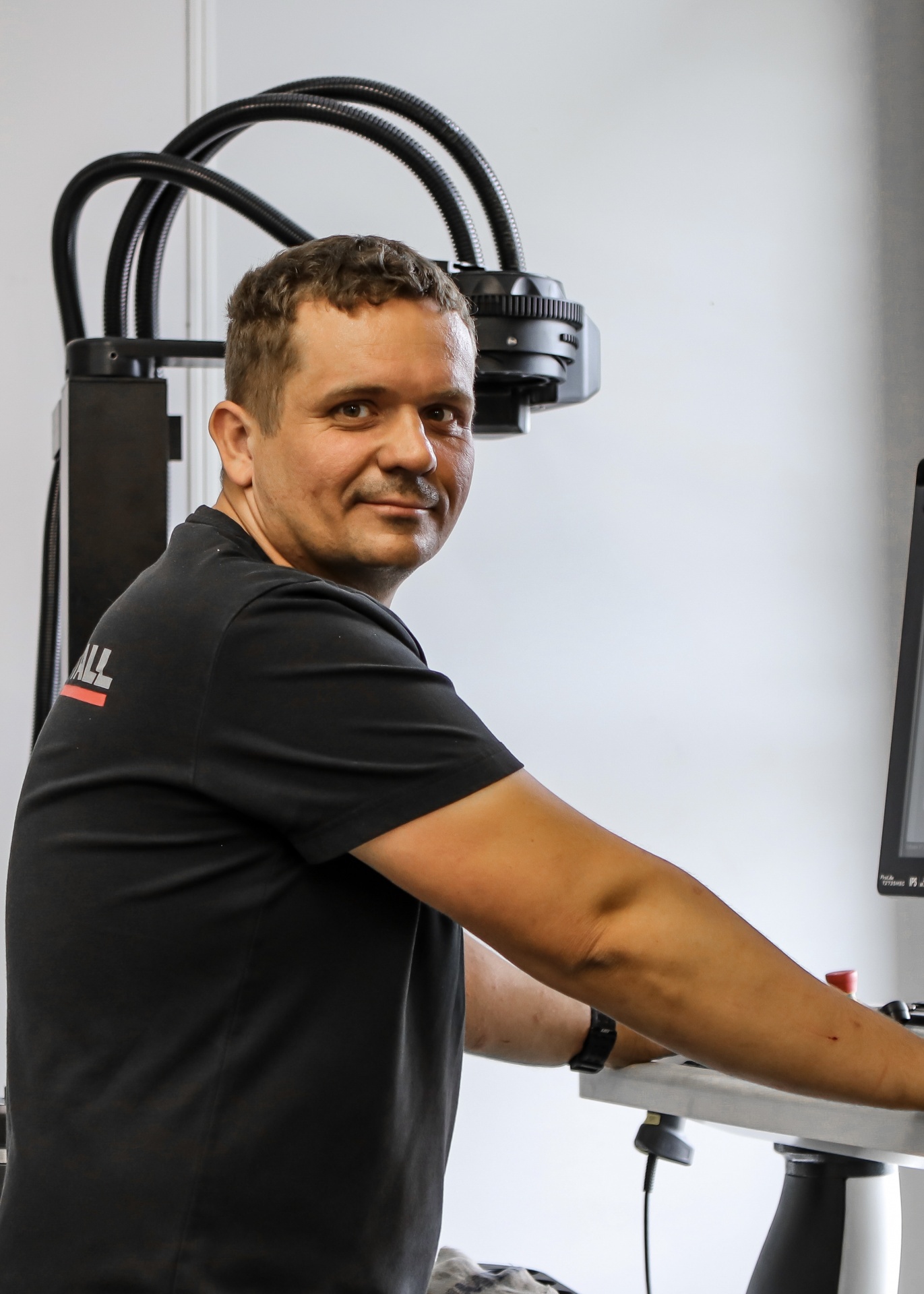 Markus (Werkzeugvorbereiter bei CUTMETALL) steht an einer Maschine und schaut über seine rechte Schulter zurück in die Kamera