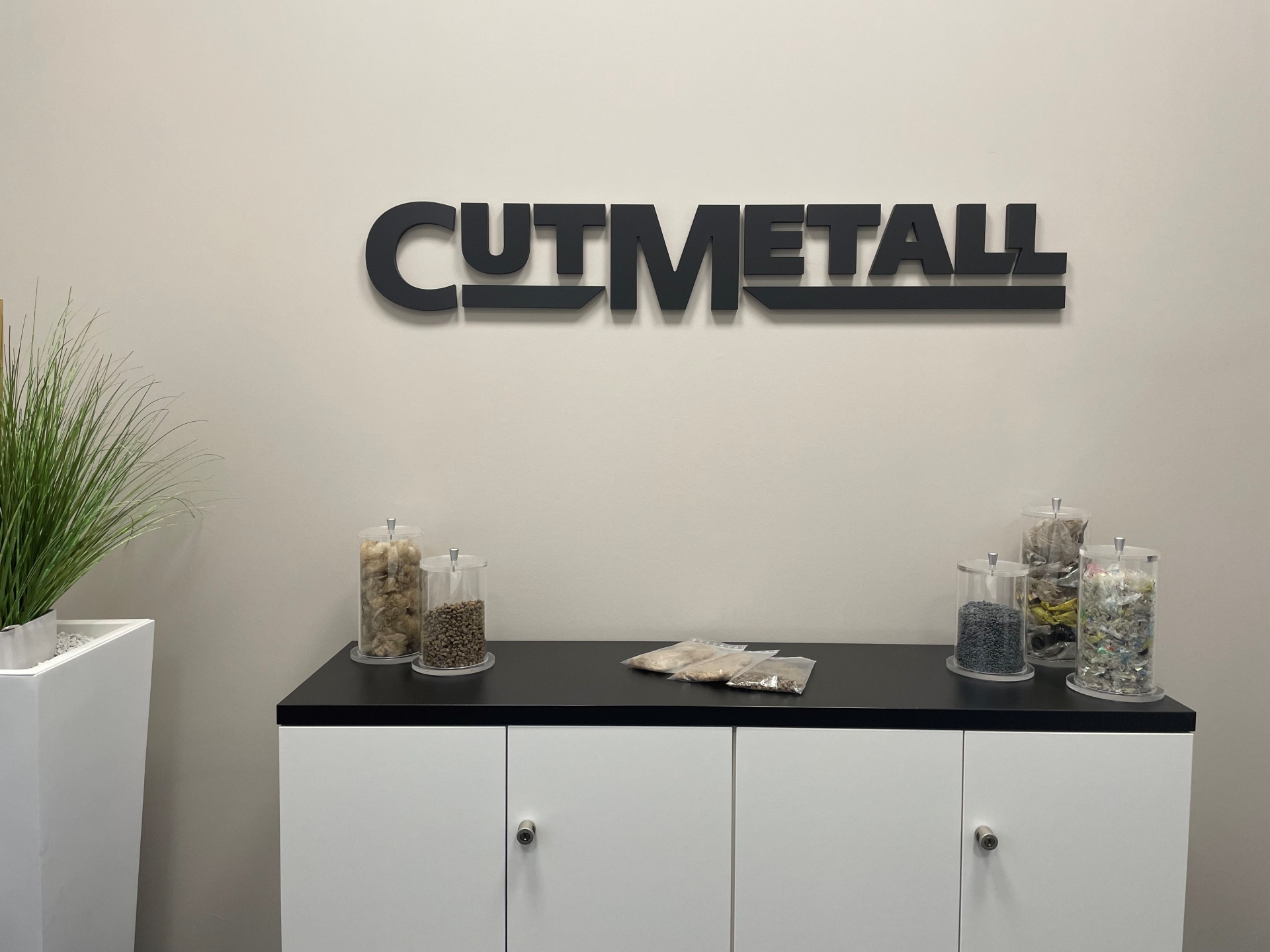 CUTMETALL Logo an der Wand im Besprechungsraum. Auf einem Schrank Gläser mit Granulat nach dem Schreddern